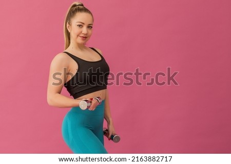 Portrait of a sports girl happy young woman in sportswear with dumbbells in her hands on a pink background. High quality photo