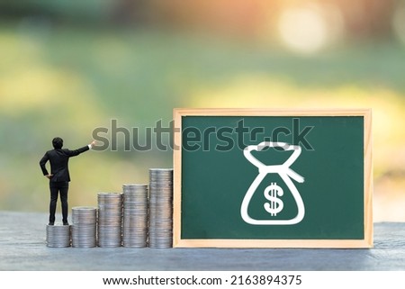 Label board the money bag of sign for saves and businessman is introducing on the stack gold coin put on the wood in the public park, Saving money and loan for business investment concept. Royalty-Free Stock Photo #2163894375