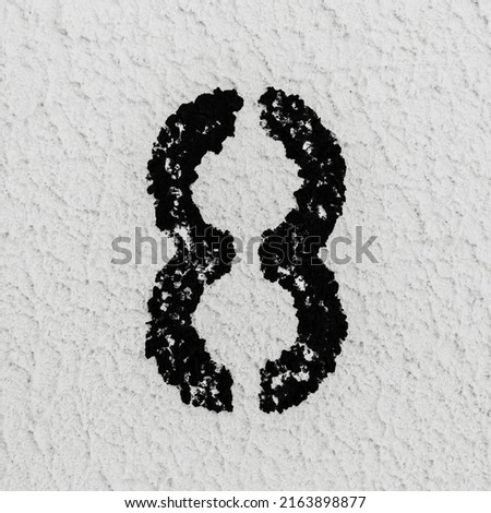 Close-up of black painted number of 8 on background of grey textured wall.