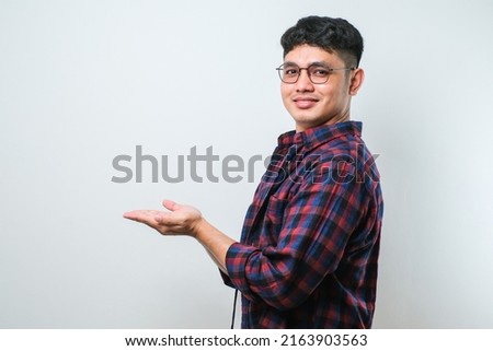 Young handsome asian man wearing casual shirt over white background with a big smile on face, pointing with hand finger to the side looking at the camera.