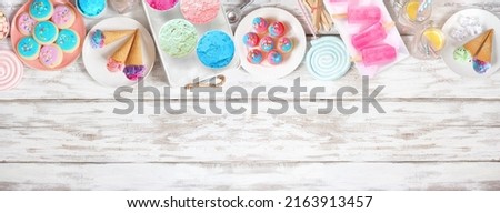 Pastel summer sweets top border. Assortment of ice cream, popsicles, cookies and treats. Overhead view over a rustic white wood banner background. Copy space. Royalty-Free Stock Photo #2163913457