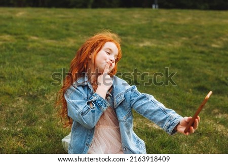 a little girl with red hair is holding a smartphone, taking a selfie. Video call concept.Modern communication.