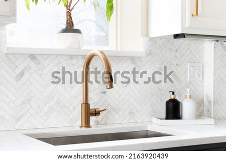 Sink detail shot in a luxury kitchen with herringbone backsplash tiles. white marble countertop, and gold faucet. Royalty-Free Stock Photo #2163920439