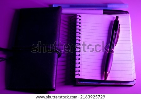 notebook and pens on purple background 