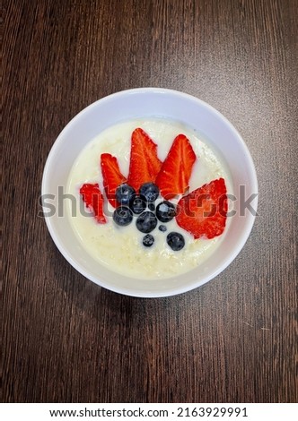 large vertical photo. milk porridge with strawberries and blueberries in a white round plate. healthy vitamin breakfast. homemade food. view from above. eco. bio. seasonal berry.