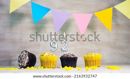 Birthday background with number 92. Beautiful birthday card with colorful garlands, a muffin with a candle burning copyspace