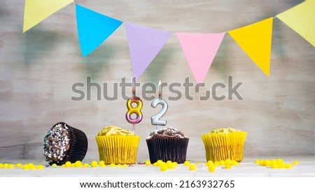 Birthday background with number 82. Beautiful birthday card with colorful garlands, a muffin with a candle burning copyspace