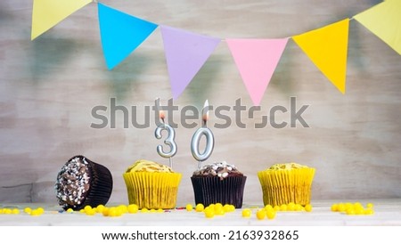 Birthday background with number 30. Beautiful birthday card with colorful garlands, a muffin with a candle burning copyspace