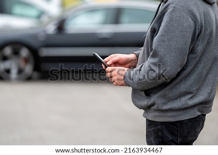 man with smartphone standing next to the car, using mobile app for online communication, shpping