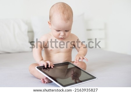 A six-month baby with a tablet computer, looking at screen, at home