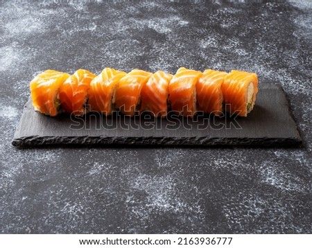 Philadelphia rolls lying on a slate serving board. Sushi roll with salmon, avocado, cream cheese on black background. Sushi menu. Japanese food.