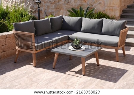 wooden corner sofa with gray pillows and table in garden 