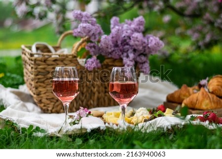 Closeup of two glass of rose wine , picnic basket, croissants, food and flowers on the grass. Banner