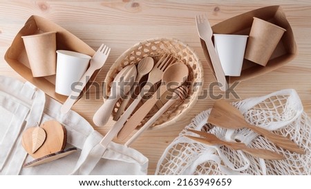Wooden cutlery, paper disposable tableware and mesh bag. Eco friendly kitchen utensils and linen shopping bag on a wooden table. Zero waste or plastic free concept Royalty-Free Stock Photo #2163949659