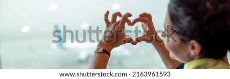 Close up of woman stewardess making heart sign with hands while looking out the window in airport terminal