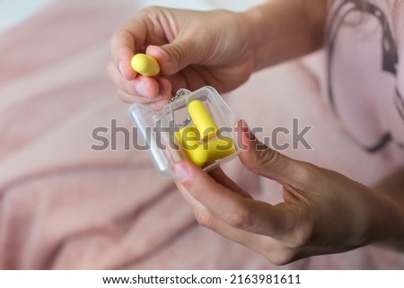 Close up of female hands and yellow earplugs. Woman holding a box of earplugs. Light background. Royalty-Free Stock Photo #2163981611