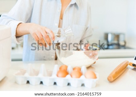 Pouring water into flour, close-up of hands of housewife cooking in the kitchen - stock photo