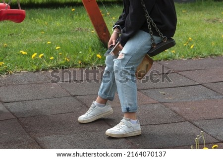 legs of a teenager sitting on a swing at the playground alone Royalty-Free Stock Photo #2164070137