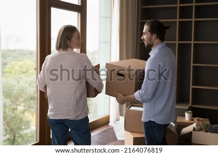 Millennial couple talking while carrying boxes with belongings into living room on move-in day, start living together in rented or bought new first property. Bank loan, tenancy, cohabitation concept Royalty-Free Stock Photo #2164076819