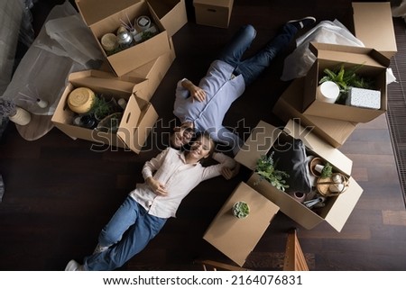 Top view happy married millennial couple relax on relocation day, ready to move out, lying on floor near stuff, personal belongings packed in big stacked cardboard boxes. New home, bank loan concept Royalty-Free Stock Photo #2164076831