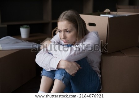 Sad young woman sits near heap of cardboard boxes with personal belongings looks upset goes through divorce, unsuccessful marriage and property division, move-out day. Eviction, mortgage debt concept Royalty-Free Stock Photo #2164076921