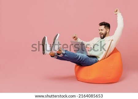 Full body young eacited overjoyed cool happy man in trendy jacket shirt sit in bag chair hold use work on laptop pc computer do winner gesture isolated on plain pastel light pink background studio. Royalty-Free Stock Photo #2164085653