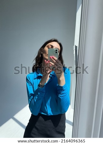 Fit tanned woman in classic short black skirt and blue blouse, take photo selfie on phone in mirror for social media, stories, vertical	