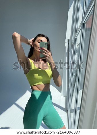 Fit tanned woman in sportswear, fitting blue leggings, perfect body, abs motivation, take photo selfie on phone in mirror for social media, stories, vertical	