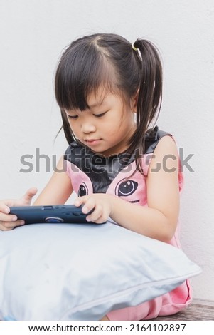 Portrait vertical image of 4-5 years old childhood. Happy Asian child girl watching and using smart phone. She laying on the bed or sofa in rest room. Leaning and using technology, social media.