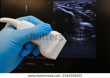 Linear ultrasound diagnostic probe held in doctor hand in blue glove, B-mode structure of wrist and median nerve for carpal tunnel syndrome diagnostics in background. Royalty-Free Stock Photo #2164106421