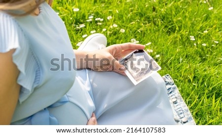 Ultrasound image pregnant baby photo. Woman holding ultrasound pregnancy picture on grass flower background. Pregnancy, medicine, pharmaceutics, health care and people concept