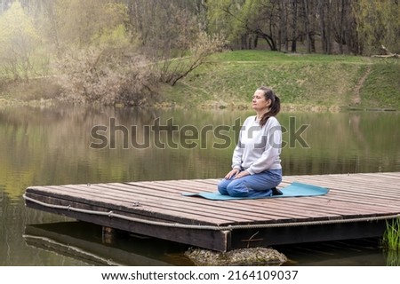 adult woman does yoga on the lake in the park