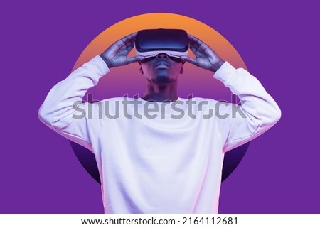 African american man looking up in vr glasses, playing video games, experiencing interactive metaverse, dressed in white mockup sweatshirt with blank copy space, isolated on violet wall with circle