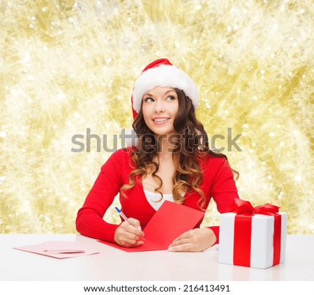 christmas, holidays, celebration, greeting and people concept - smiling woman in santa helper hat with gift box writing letter or sending post card over yellow lights background