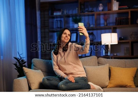 Portrait of a beautiful smiling woman making selfie photo on smartphone. Home leisure in the evening, cinematic lighting