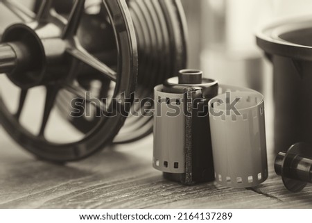 Photo film roll and cassette, photographic equipment - developing tank with its film reels on background. Selective focus. Retro black and white photo.