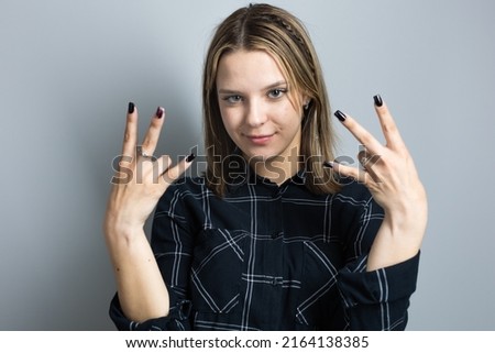 Beautiful teenager girl emotionally gesticulates with her hands on a gray background