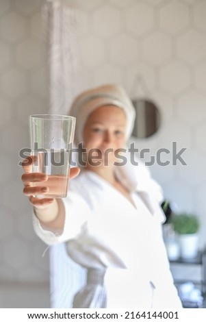 in the foreground a caucasian female hand holds a glass of clean water, gives the camera a smile. The concept of a healthy lifestyle, beauty skin care Royalty-Free Stock Photo #2164144001