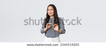 Lifestyle, beauty and fashion, people emotions concept. Reluctant and disgusted asian woman tell to stay away from her, step back and raising hands up defensive, grimacing from aversion and dislike Royalty-Free Stock Photo #2164154203