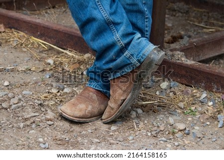 Pair of men's cowboy boots and denim jeans standing in the dirt.