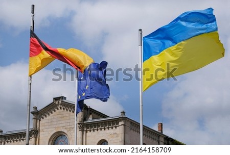 The flag of Ukraine waving in the wind, while the German and flags are entangled