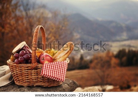Wicker picnic basket with different products on rock in mountains. Space for text