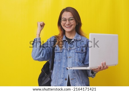 Successful young asian college student standing while holding laptop and clenching her hand