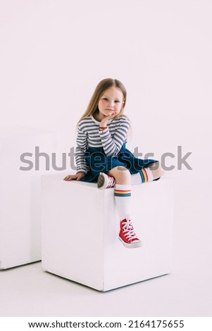 Calm, smiling. One little cute Caucasian girl in white summer clothes sitting on big box isolated over white studio background. Copyspace for advertisement