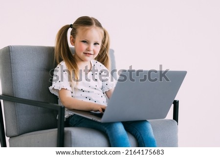 Portrait of little girl study online with laptop while sitting black chair on white background.