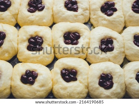 Raw buns with cherries in a glass form, close-up, top view

