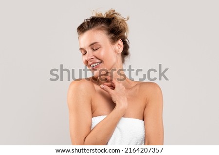 Self-Pampering Concept. Middle Aged Woman Wrapped In Bath Towel Touching Her Skin While Standing Over Light Gray Background, Attractive Mature Lady Enjoying Beauty Treatments, Copy Space Royalty-Free Stock Photo #2164207357