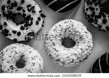Flat lay image of ring donut with white glaze and hundreds and thousands amids other donuts, black and white image 