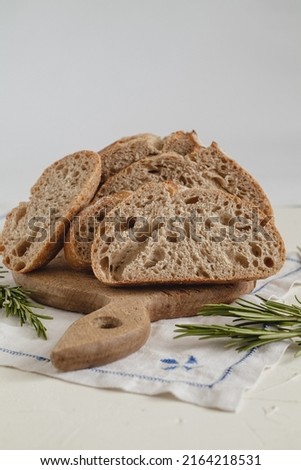 Fresh sliced rye bread close up on a wooden board, knife and rosemary on a white background.