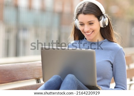 Happy teen with wireless headphones using laptop in a park